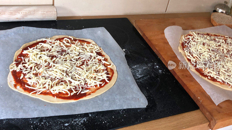 这是一款准备在厨房热烤箱中烘烤的未煮的自制披萨，自制的那不勒斯玛格丽塔/玛格丽塔披萨浓郁的番茄酱，意大利调味香草，磨碎的马苏里拉芝士，不粘防油纸/羊皮纸，木制擀面棍